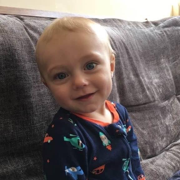 Baby Elijah smiling on the couch in helicopter pajamas